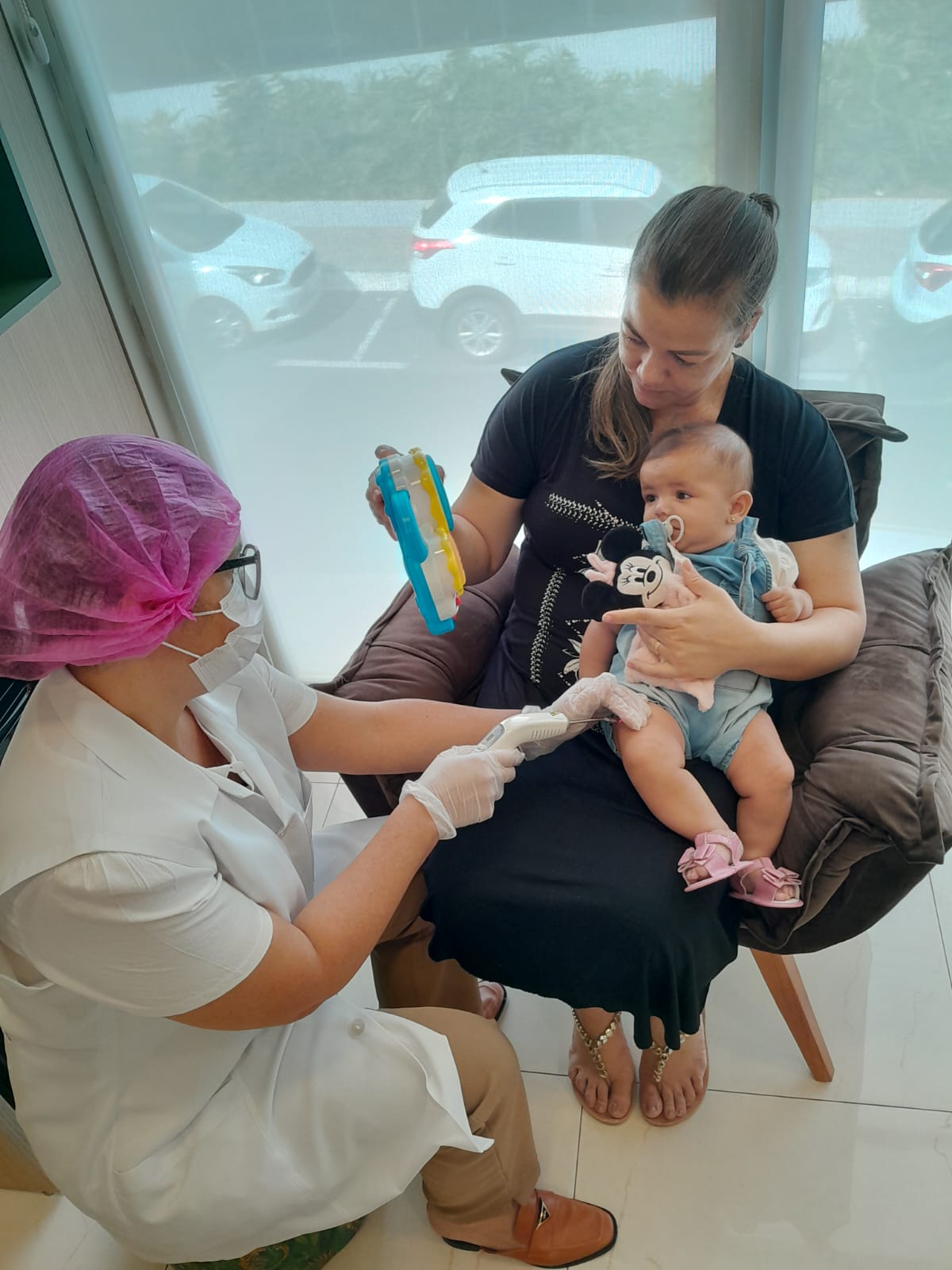 Profissional da Proteja aplicando laser pós-vacina em bebê no colo da mãe em Catalão